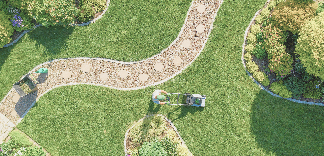Aerial view of man in green hat and gloves mowing manicured landscape